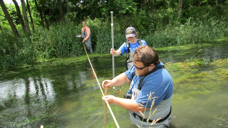 Three summer interns measuring stream parameters.