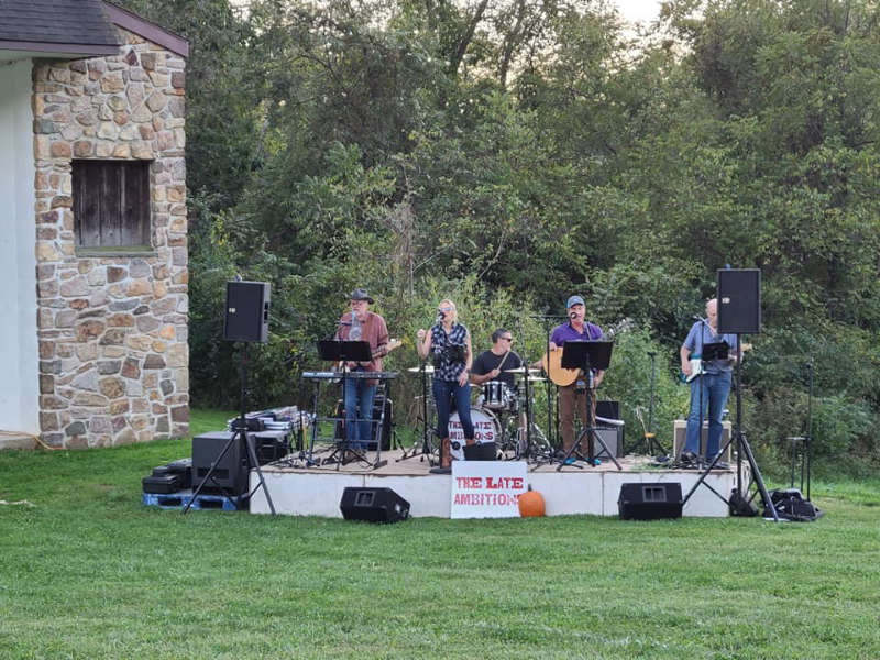 The Late Ambitions band playing on an outdoor stage.