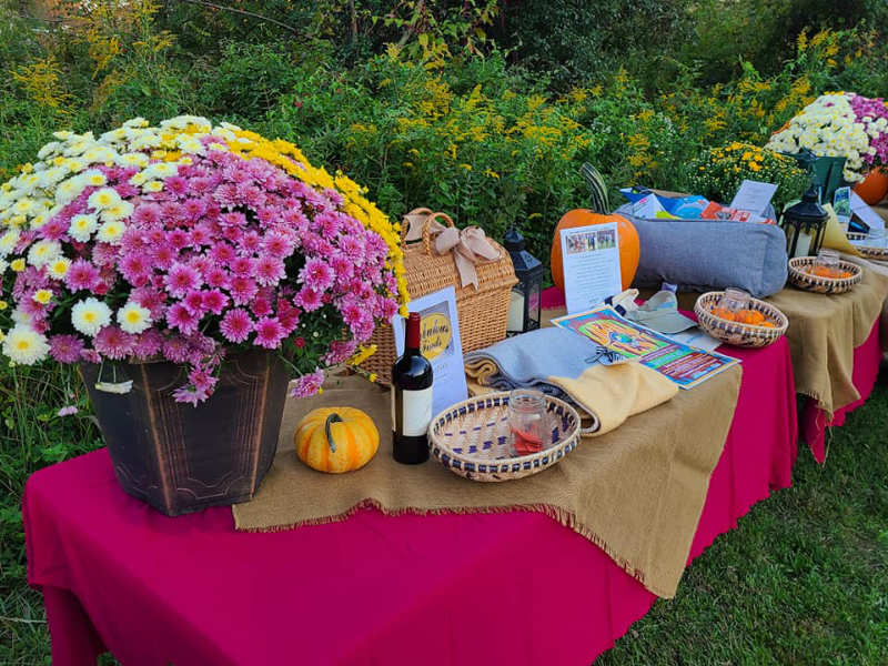 Colorful mums and pumpkins decorate a table of raffle items at an outdoor festival.