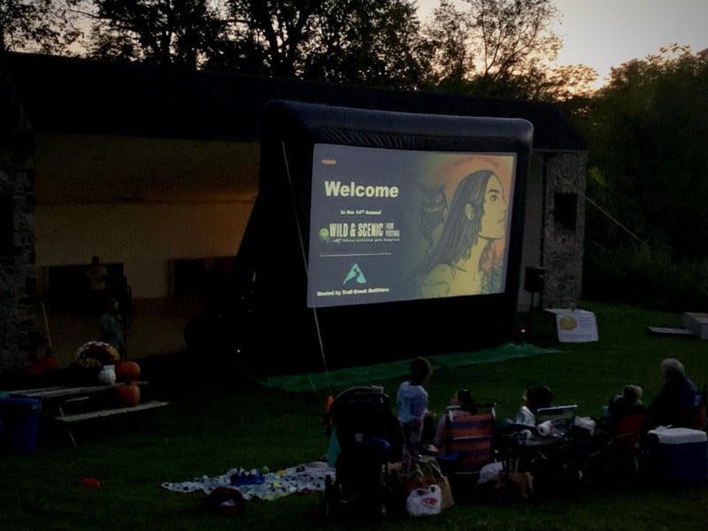 Audience watching films on an outdoor screen at sunset.