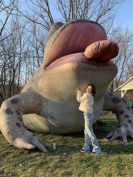 A girl smiles next to a giant inflatable frog.