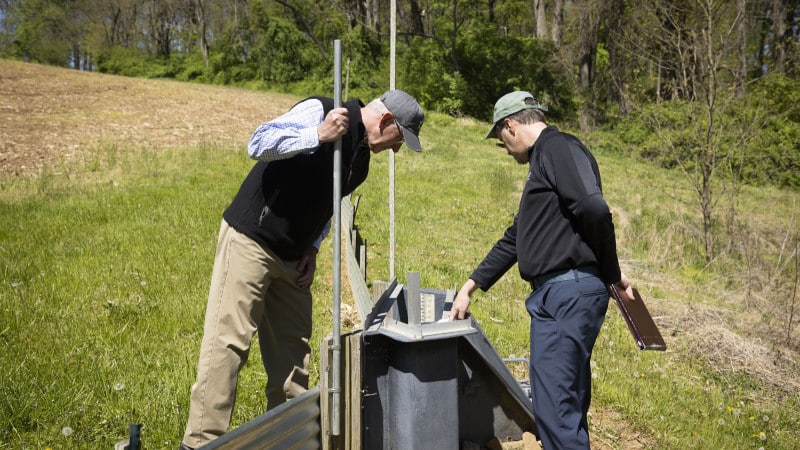 Two men look at an experimental flume on the edge of an agricultural field.