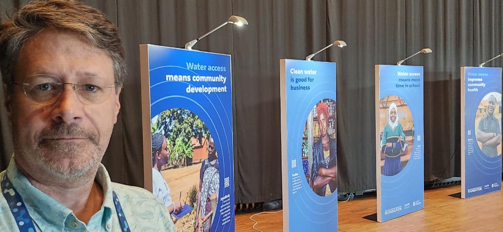 Dave Arscott at World Water Week 2024, next to large signs with photos and text about clean water access.