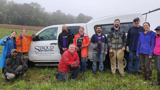 A group of Exelon volunteers lean against a Stroud Center truck at a tree planting event.