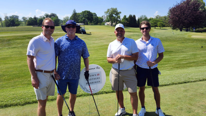 Golfers next to a Brown Brothers Harriman sponsorship sign.