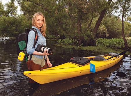 Alexandra Cousteau holding a camera and standing in water next to a kayak.
