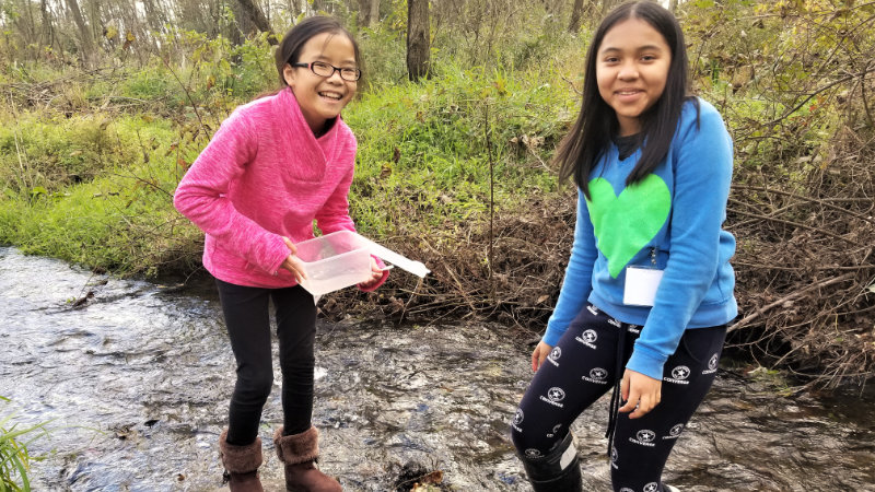 Two girls take a stream sample.