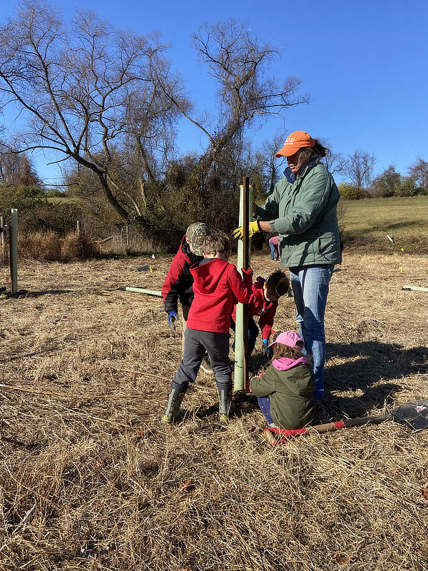 Kids help plant a tree in a New Bolton Center buffer.