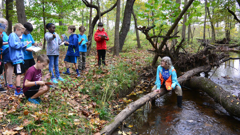 An educator prepares to release a rubber duck in a stream to demonstrate stream velocity.
