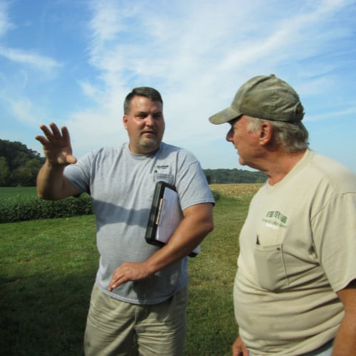 Two men talking in a farm field.