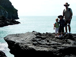 Dave Arscott stands with his children on a rocky ledge at Godley Head.