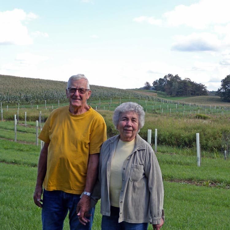 A man and woman stand in front of a newly planted riparian buffer on a farm.