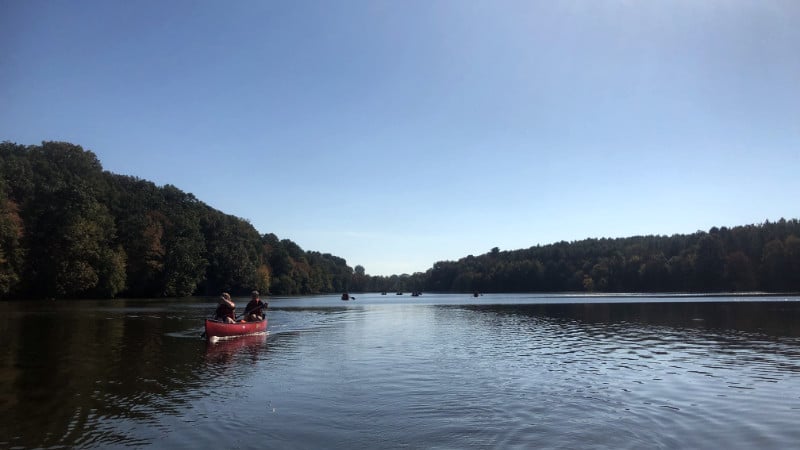 Two people paddling a red canoe on Octoraro Reservoir, with other canoes in the distance.