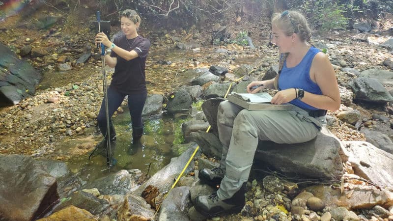 Two scientist collecting and recording data in a stream.