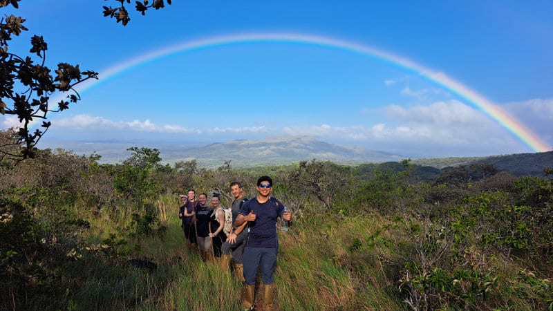 College students on a hike in Costa Rica smile as a rainbow arches overhead.