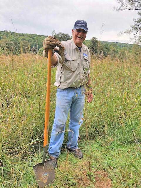 Photo of Dean Neely with a shovel surrounded by tall grass