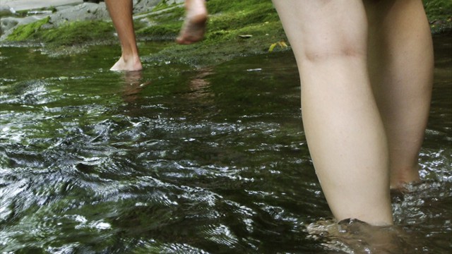 Trekkers cross a shallow creek barefoot.