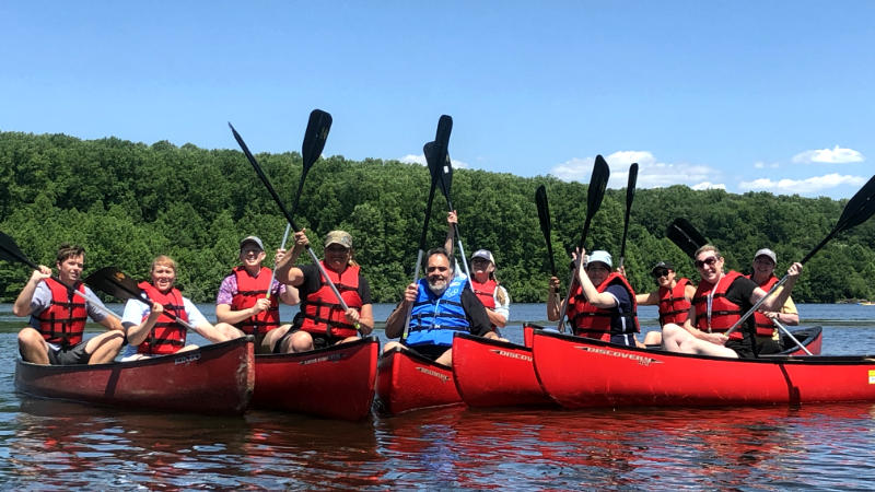 Ten educators wearing red life vests in red canoes on a calm body of water.