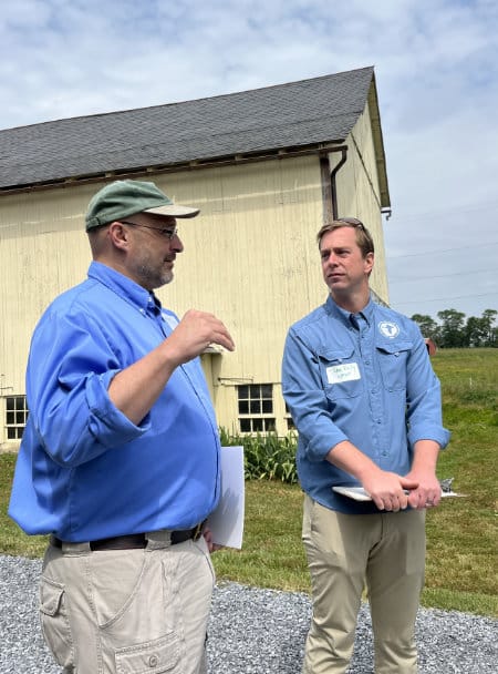 Two men discussing a farm tour in front of a barn.