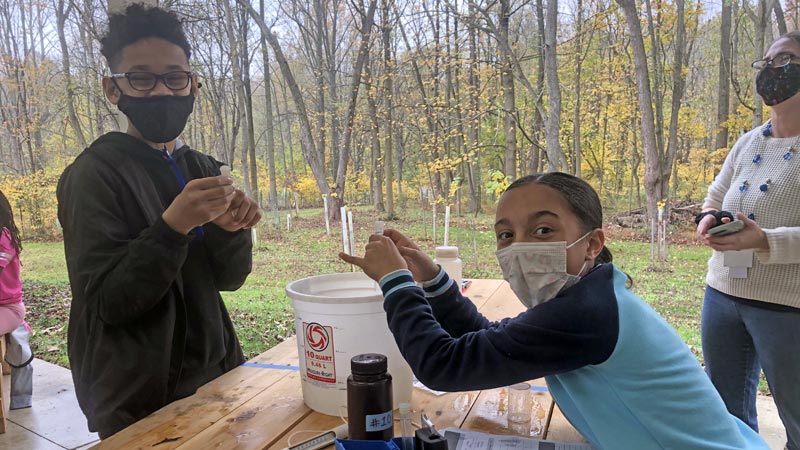 Two elementary school students wearing face masks and performing stream water chemistry tests.