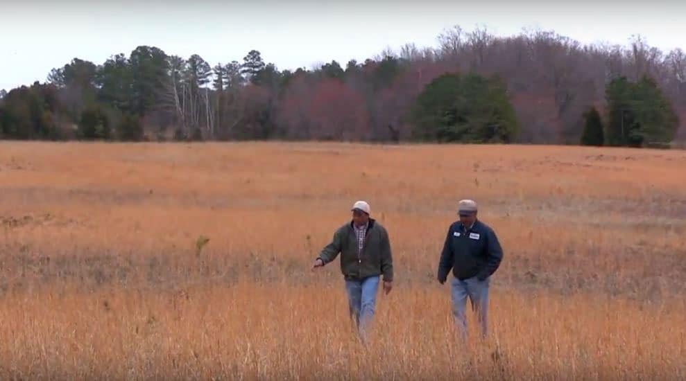 Two farmers walk across a field in winter.