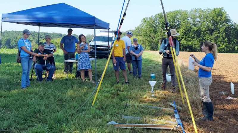 Melinda Daniels stands at the edge of a farm field and explains to a small group how a rainfall simulator works.