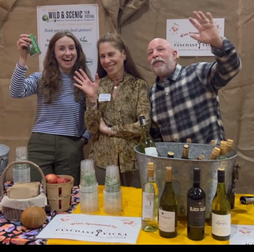 Three people wave while standing behind a table with wine and beer for film festival attendees.