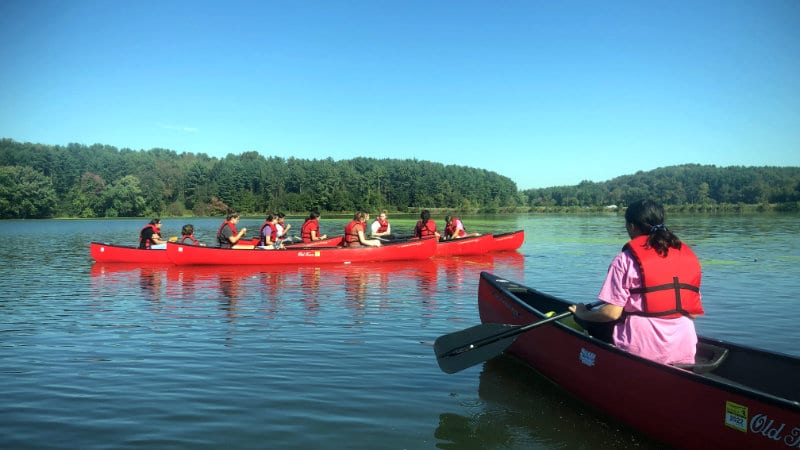 A troop of Girl Scouts in five red canoes on a lake.
