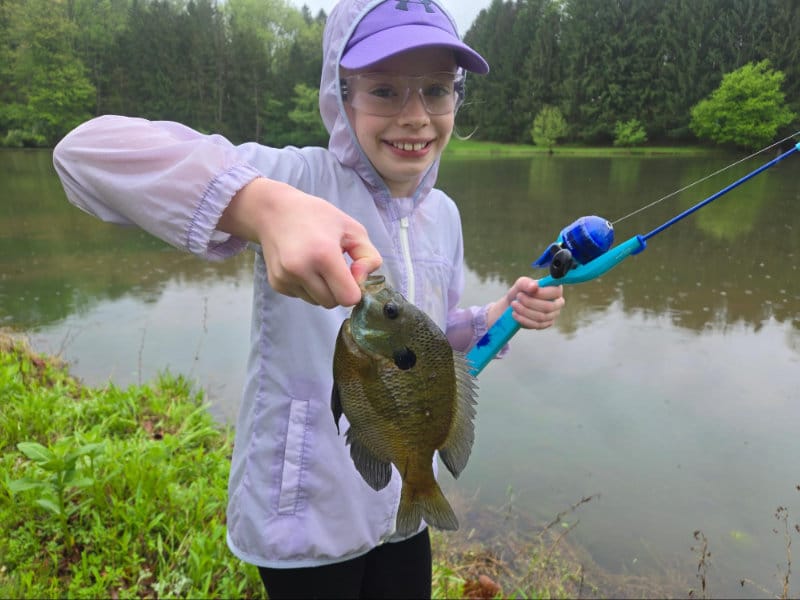 A girl smiles while holding a bluegill fish she caught.