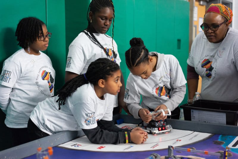 Four girls and an adult mentor from the Harambee Institute robotics team.