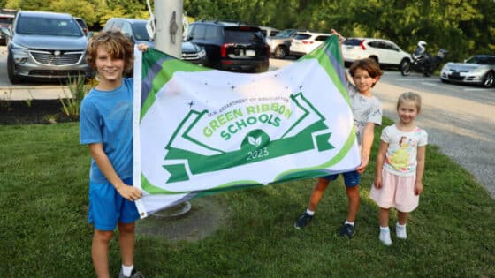 Three children hold Hillendale Elementary School's 2023 Green Ribbon Schools flag.