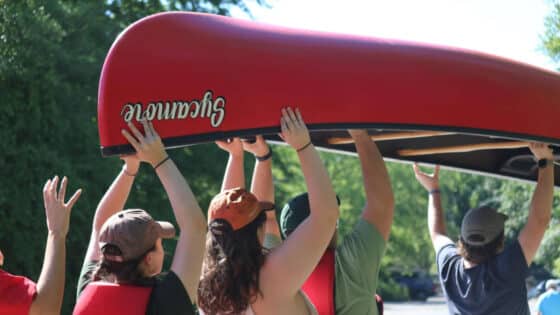 Summer interns carrying a canoe over their heads.