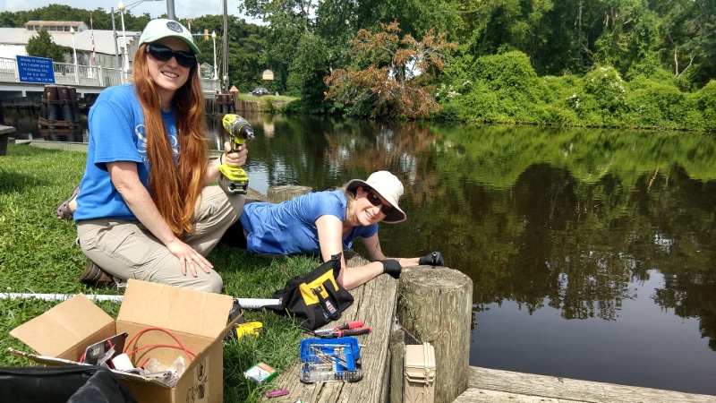 Rachel Johnson and Shannon Hicks install an EnviroDIY Monitoring Station on a river piling.