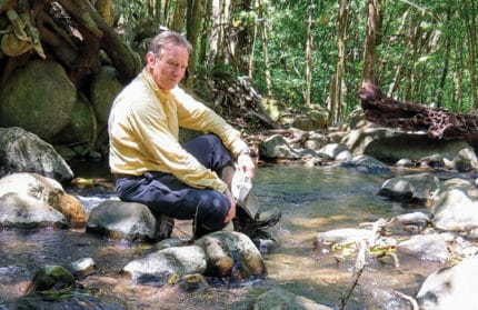 Photo of Lou Kaplan seated on a rock in a stream