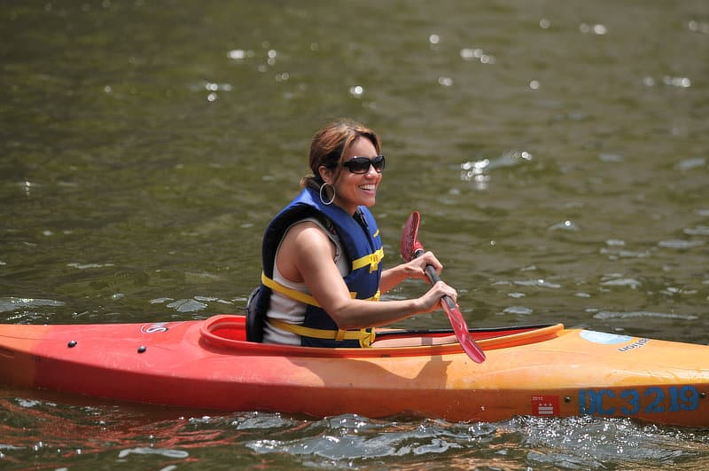 A smiling woman paddles an orange kayak.