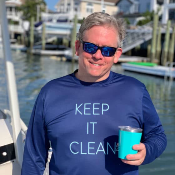 A man on a dock wearing a sun protection t-shirt with long sleeves and the words Keep It Clean.