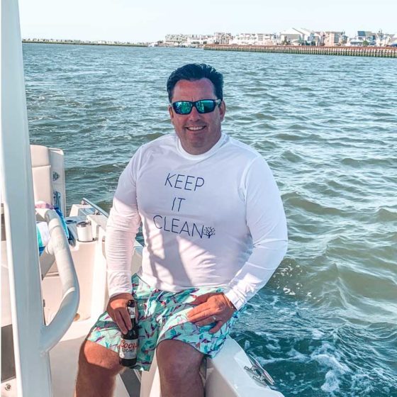 A man on a boat wearing a long-sleeved sun protection shirt with the words Keep It Clean.