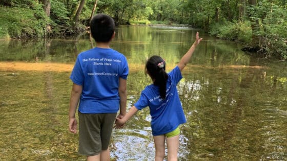 Two kids hold hands while walking in a creek.