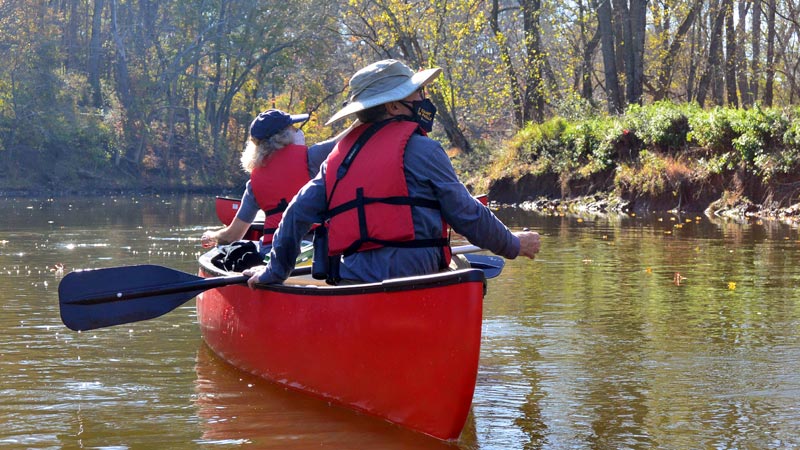 A man and woman pictured from the back, paddling in a red canoe.