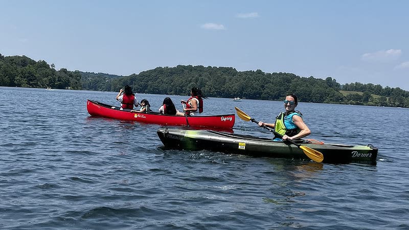 An educator in a kayak instructs a family in canoeing technique.