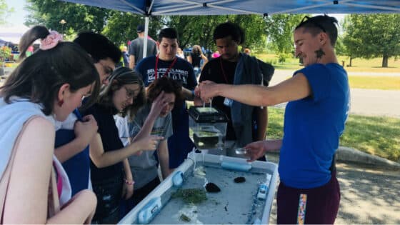 An educator shows aquatic macroinvertebrates to a crowd at the touch tank.