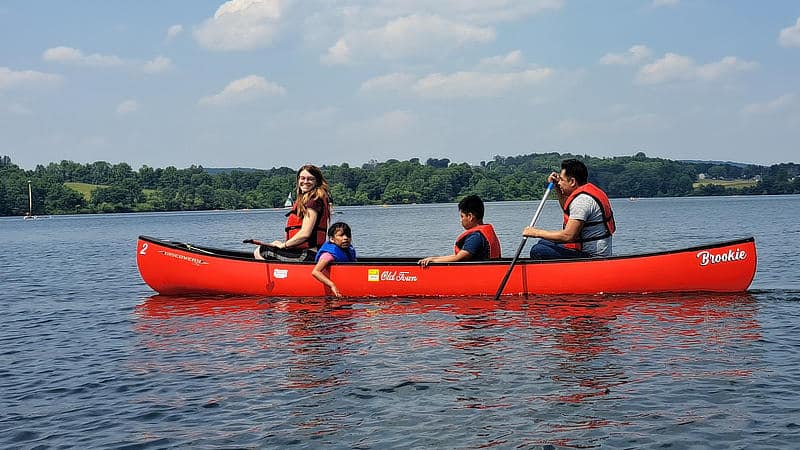 A family of four paddles a red canoe on a lake.