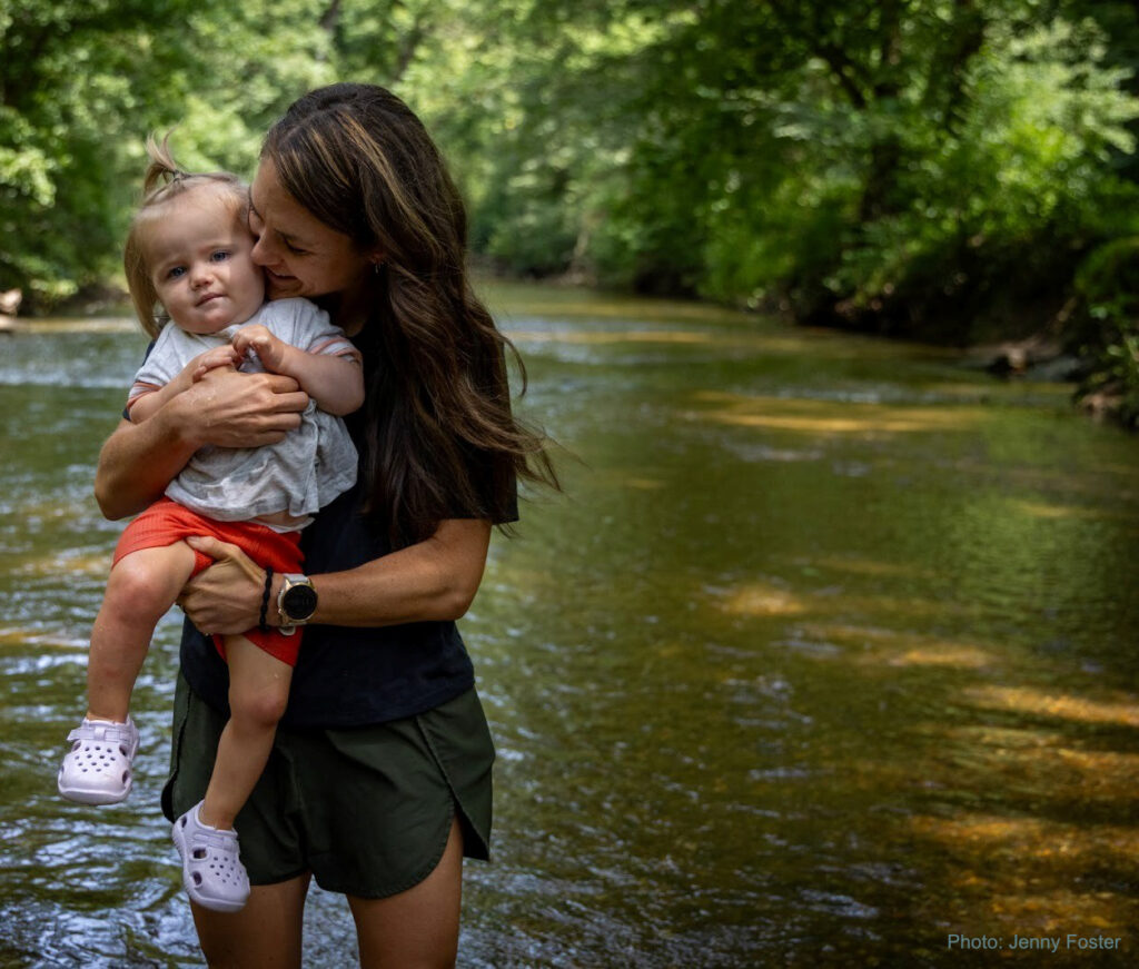 A woman hugs a small child while standing in a river.