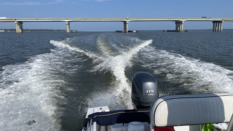 A motor boat on the Choptank River, with its wake and a bridge in the distance.