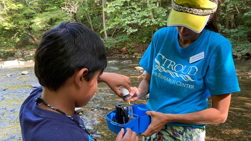 Tara Muenz helps a child test the pH of a stream water sample.