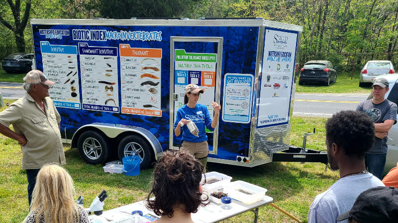 Woman explains the Leaf Pack Network to volunteers near the Watershed Education Mobile Lab.