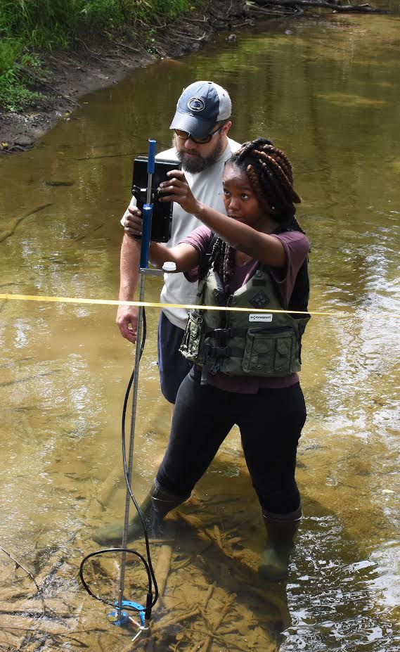 Myriah Wadley using scientific instrumentation while standing in a stream.