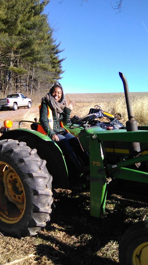 Myriah Wadley sitting on a tractor on the edge of a farm field.