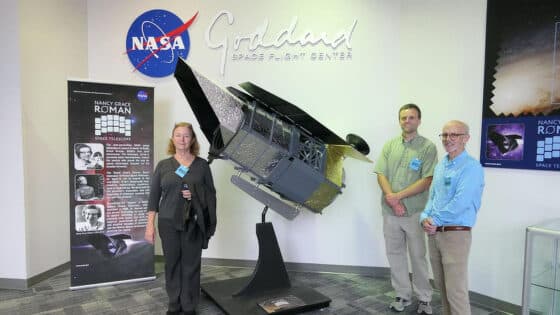 Three people next to a replica of the Nancy Grace Roman space telescope at the Goddard Space Flight Center.