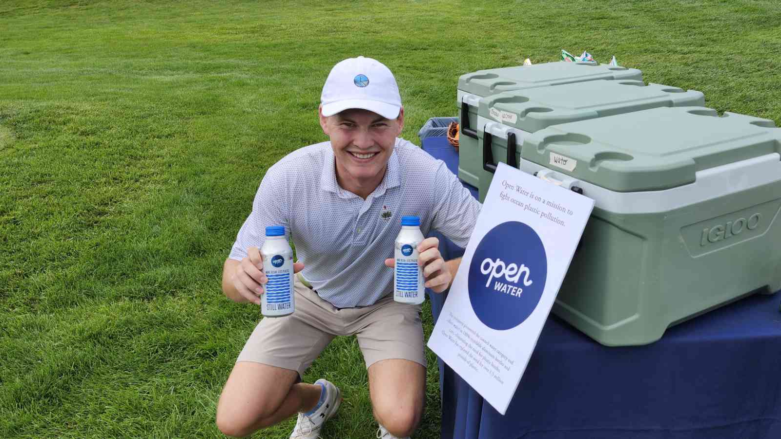 A young man holds Open Water brand canned water near a golf course.